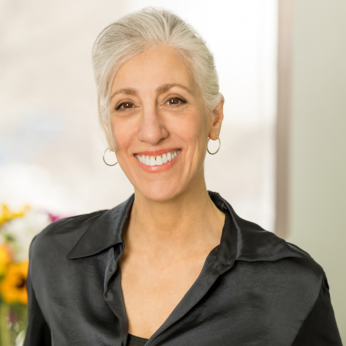 A woman in a dark shirt, with bright backgroiund, smiles.