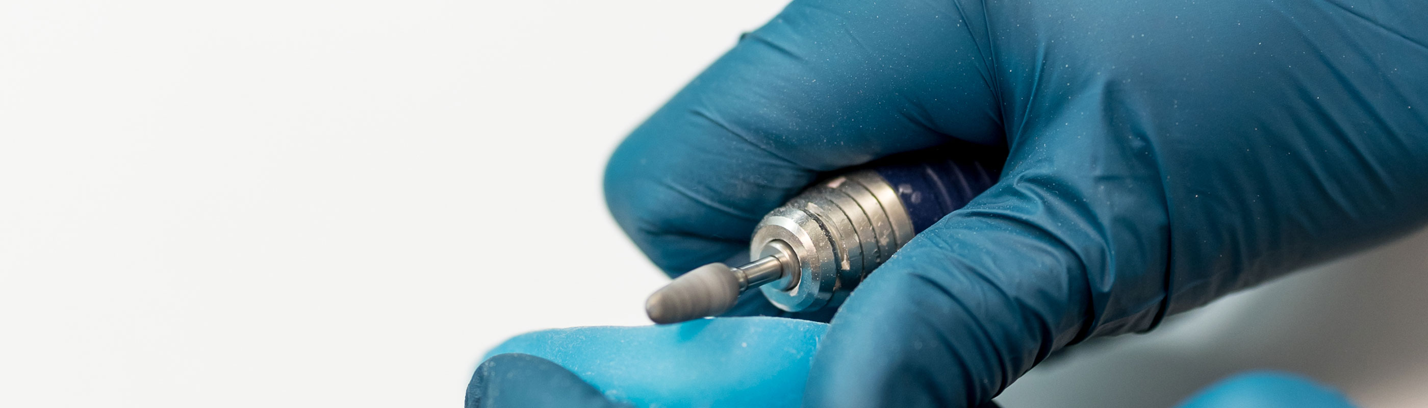 A blue medical gloved hand works with a dentists tool to build a model.