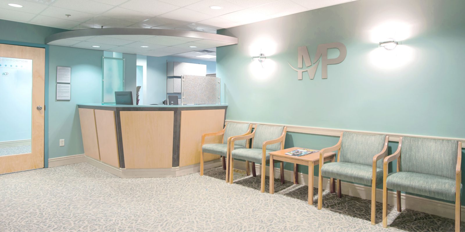 A softly lit waiting room with colors of teal and blue, wood chairs line the wall.