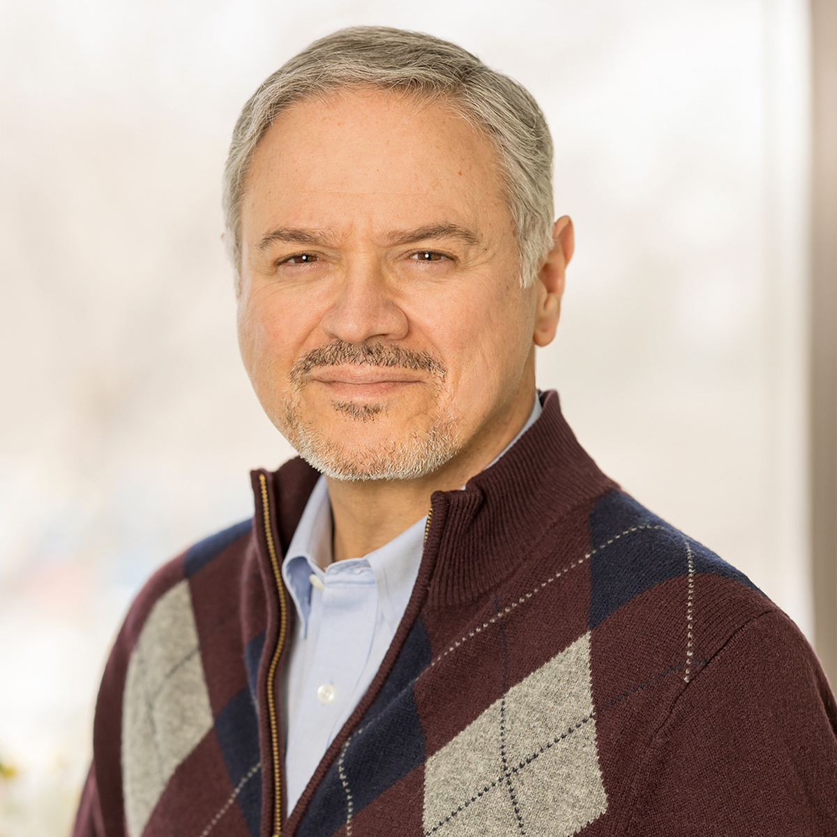 A man in a dark sweater and and collared shirt smiles at the camera.